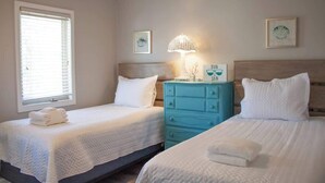 Habitación de hotel con dos camas, un aparador azul, una lámpara y cuadros en las paredes.