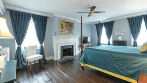 Un dormitorio con una cama grande, una chimenea, un ventilador de techo y una silla.