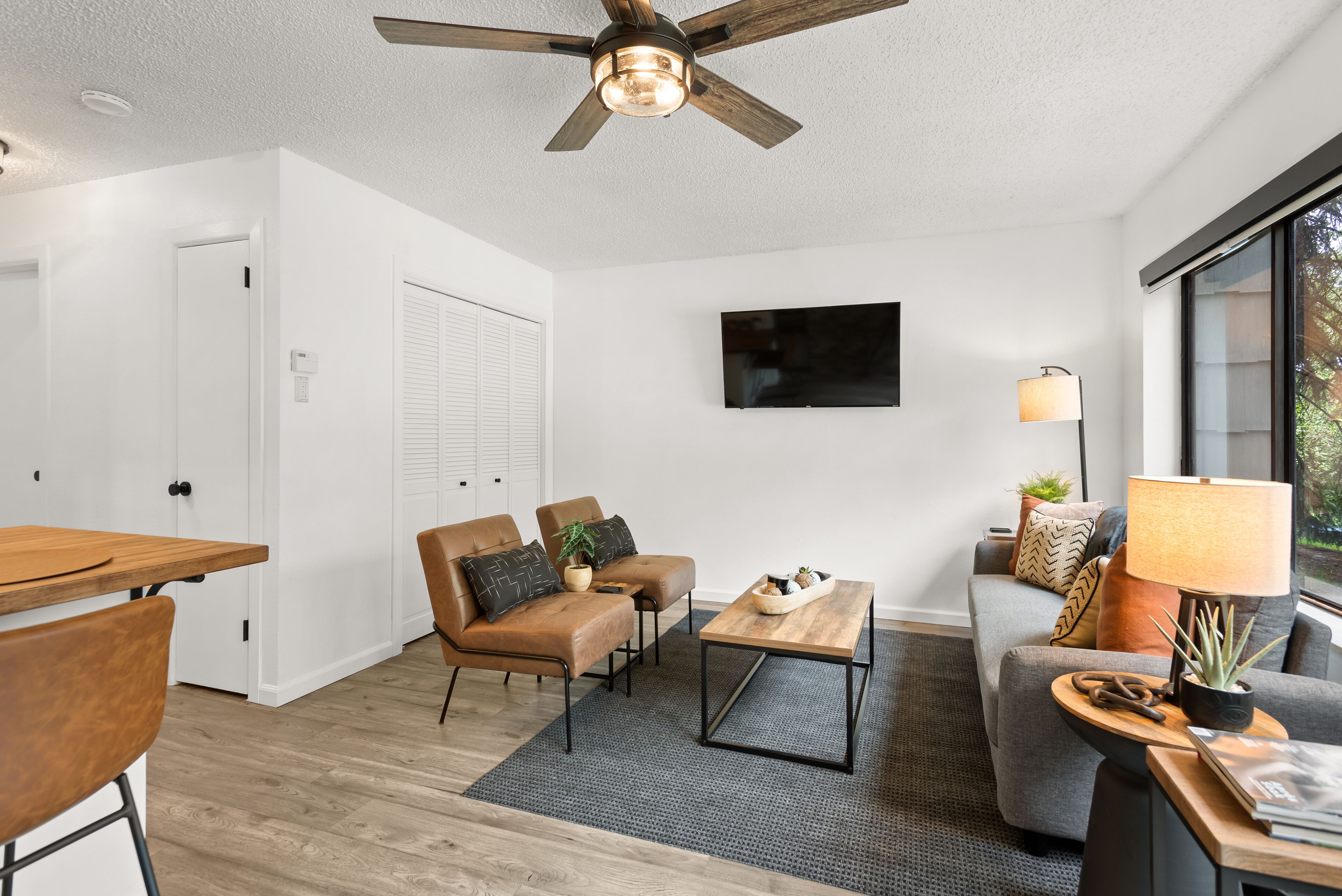 A modern living room with a ceiling fan, a flat-screen TV, a wooden coffee table, and a grey sofa.
