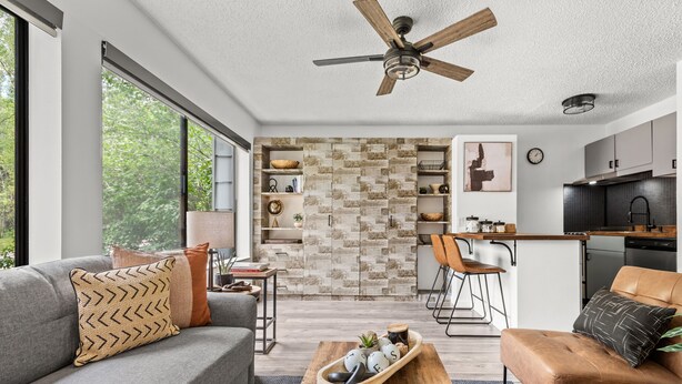 A modern living room with a grey sofa, a wooden coffee table, and a brown leather chair. A kitchen is visible in the background with a stone backsplash and wooden cabinets. - HOLT - Billionaire Mountain (Aspen)
