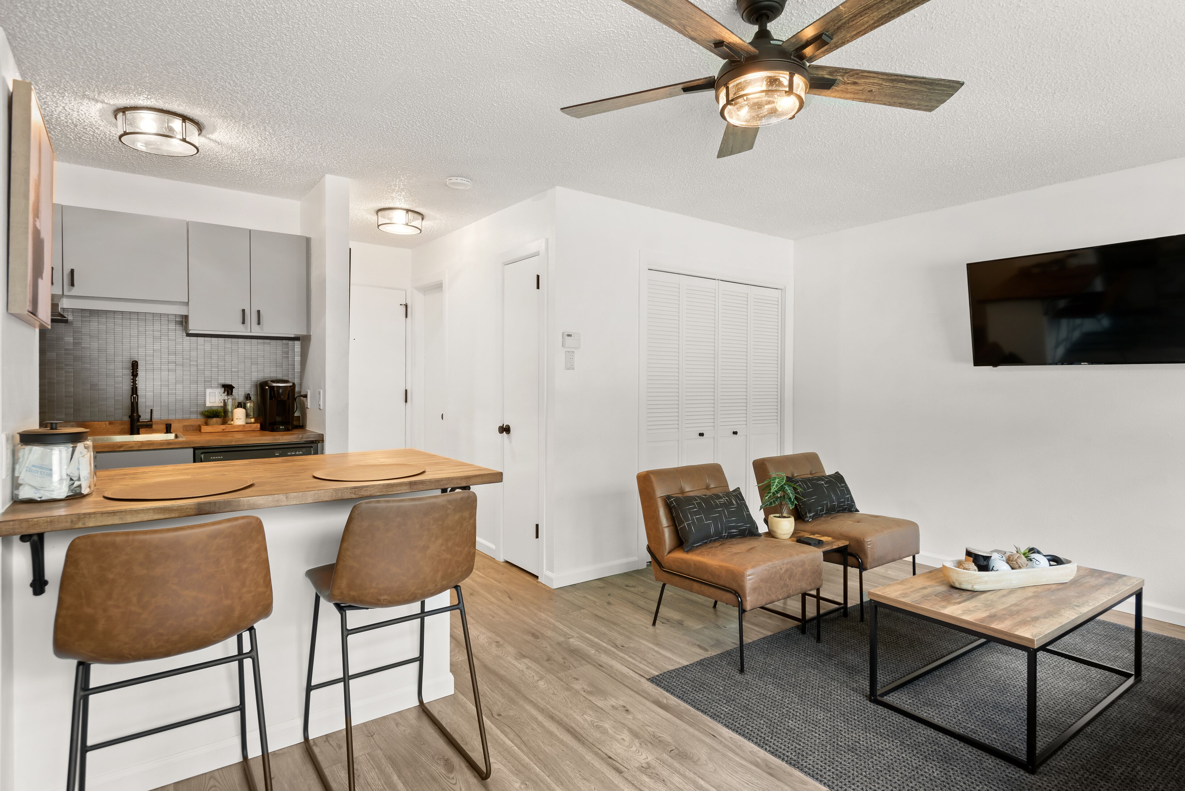A modern kitchen with a wooden countertop, bar stools, and a ceiling fan.