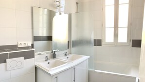 A modern bathroom with a white sink, mirror, and toilet. There is a window providing natural light and a towel rack above the sink. - House (Arcueil)