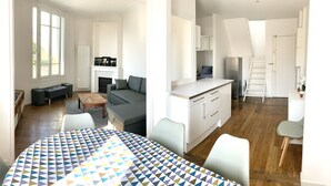 A spacious living area with a fireplace, a dining table, and a kitchen with white cabinets. - House (Arcueil)