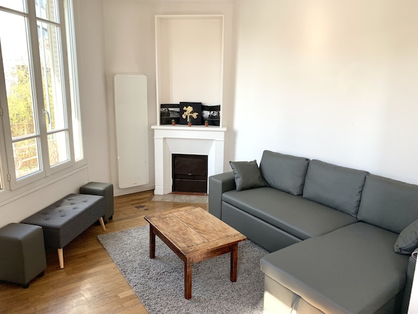 A modern living room with a grey sofa, a wooden coffee table, a grey bench, and a fireplace with decorative items.