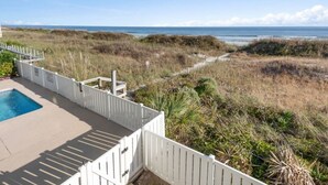 Un espace piscine entouré d’une clôture blanche, offrant une vue dégagée sur la plage, et un chemin menant à la plage.