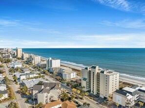 Un hôtel situé sur la côte, composé de plusieurs bâtiments, offrant une vue sur la plage et bénéficiant d’un ciel dégagé.