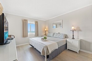 Een slaapkamer met een bed, nachtkastjes, een televisie en een raam met gordijnen.