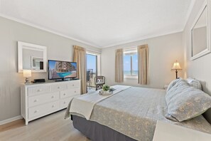 Een slaapkamer met een bed, een televisie, een dressoir en een raam met gordijnen.