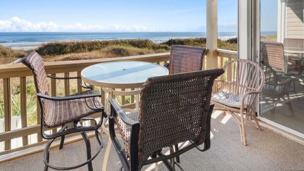 Un balcon avec des fauteuils en osier, une table en verre et une vue sur l’océan.