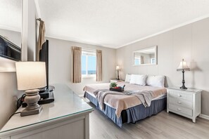 Une chambre d’hôtel comprenant un lit, des tables de chevet, un bureau, une lampe, un miroir et une fenêtre avec des rideaux.