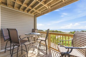 Une terrasse en bois, aménagée avec du mobilier d’extérieur, notamment des chaises et une table, donnant sur une plage.