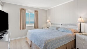 Une chambre à coucher avec un lit, des tables de chevet, un téléviseur et une fenêtre avec des rideaux.