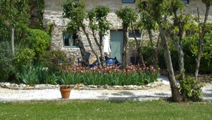 Ein Gebäude aus Stein mit einem Ziegeldach, umgeben von Bäumen und einem Blumenbeet.