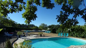 Ein Schwimmbecken mit Steinrand und Liegestühlen darum herum.