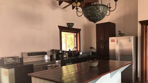 Een keuken met een centraal eiland, houten kasten, een roestvrijstalen koelkast en een hangende kroonluchter.
