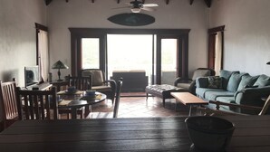 Een ruime woonkamer met een eettafel, stoelen, een bank en een plafondventilator.