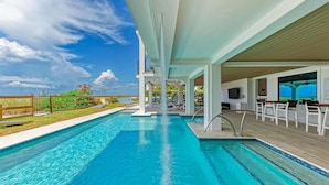 A swimming pool with a waterfall feature, lounge chairs, and a covered seating area. - Buena Vista #2: Luxury Beach Front Condo, Amazing Views, Pool by Anna Maria Life Vacation Rentals (Holmes Beach)