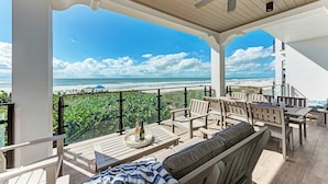 A covered outdoor seating area with a view of the beach, featuring a ceiling fan, tables, and chairs. - Buena Vista #2: Luxury Beach Front Condo, Amazing Views, Pool by Anna Maria Life Vacation Rentals (Holmes Beach)