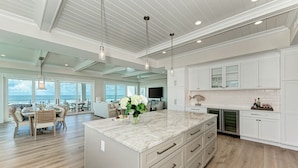 A spacious kitchen with a large island, white cabinetry, and a view of the ocean. - Buena Vista #2: Luxury Beach Front Condo, Amazing Views, Pool by Anna Maria Life Vacation Rentals (Holmes Beach)
