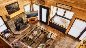 Interior acogedor de una cabaña con chimenea, un ventanal grande, un sofá y una bañera.