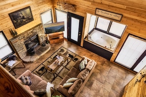 A cozy cabin interior with a fireplace, a large window, a sofa, and a bathtub.