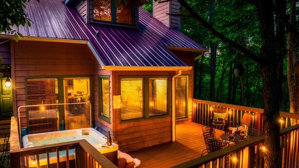 Terraza de madera con jacuzzi, asientos al aire libre y luces colgantes.