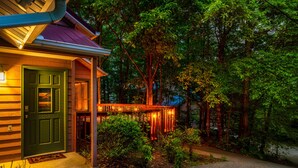 Una casa de madera con puerta verde, un porche con luces colgantes y zona arbolada.
