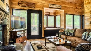 Interior acogedor de una cabaña con chimenea de piedra, paredes de madera, un sofá de cuero y una mesa de comedor con una copa de vino.