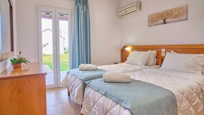 Hotellihuone, jossa on kaksi sänkyä, puinen pääty, ruukkukasvi ja näkymä ulos.
