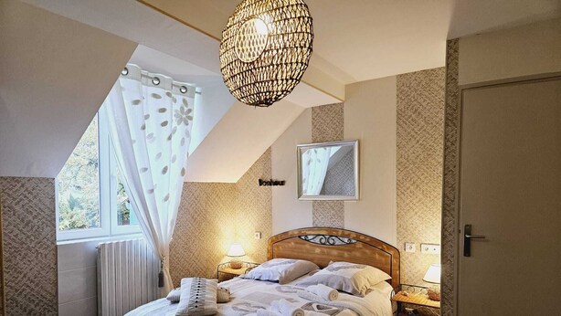 A bedroom with a bed, bedside lamps, a hanging light fixture, a window with curtains, a door, and a mirror on the wall. - *** Family Room Au petit bonheur (Gramat)