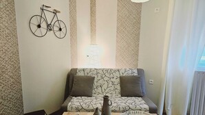 A living room with a sofa, a coffee table, a wall-mounted bicycle, and patterned wallpaper. - *** Family Room Au petit bonheur (Gramat)