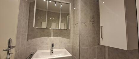 Une salle de bain avec un lavabo blanc, un miroir et un espace douche.