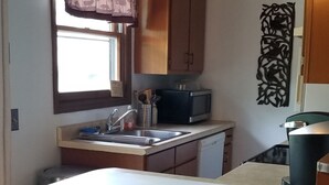 Une cuisine compacte dotée d’un plan de travail en bois, de deux tabourets, d’un évier et d’un four à micro-ondes.
