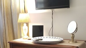 Une commode en bois avec des tiroirs, un téléviseur fixé au mur, une lampe et un miroir posé sur la commode.