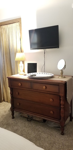 A wooden dresser with drawers, a television mounted on the wall, a lamp, and a mirror on the dresser.
