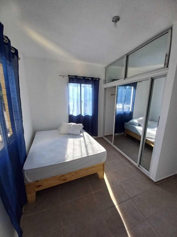 Une chambre à coucher avec un lit, une fenêtre avec des rideaux, une porte-fenêtre coulissante et un luminaire au plafond.