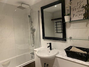 Un baño con ducha envuelta en vidrio, un lavabo blanco y un espejo encima.