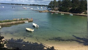 A coastal scene with boats docked at a marina, clear water, and a sandy beach with trees. - Sea view house (56780 - ILE AUX MOINES)