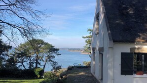 A house with a stone pathway leading to a white building with black shutters, overlooking a body of water. - Sea view house (56780 - ILE AUX MOINES)
