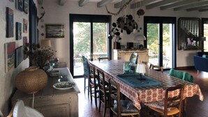A dining area with a long table, chairs, a vase, and a lamp. There are windows and a view of the outdoors. - Sea view house (56780 - ILE AUX MOINES)