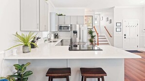 Uma cozinha moderna com armários brancos, uma ilha central com banquetas, eletrodomésticos de aço inoxidável e uma escada que leva a outro andar.
