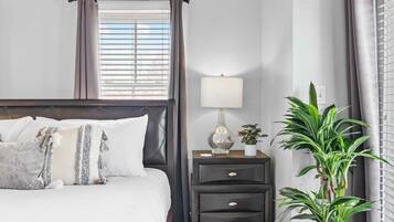 Un dormitorio ordenado con una cama, mesitas de noche, una lámpara y una planta en maceta.