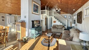 A spacious living area with a wooden ceiling, a staircase, a fireplace, and a sofa.