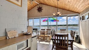 A kitchen with a view of the water, wooden ceiling, and a dining area with chairs and tables.
