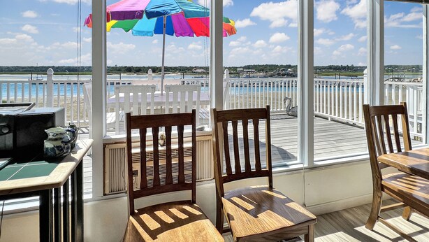 A covered outdoor seating area with white railings, wooden chairs, and a colorful umbrella.