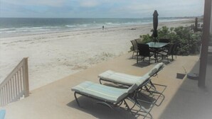 A beach view with lounge chairs and a table, a wooden fence, and a clear sky. - Sea Breeze - W007 Wonderful Beachfront Oceanfront property for the whole family (Wells)