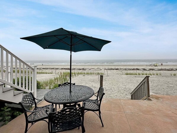 A patio with a table and chairs, an umbrella, and a view of the beach.