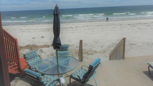 A beachside patio with a glass table and chairs, a black umbrella, and a view of the ocean. - Sea Breeze - W007 Wonderful Beachfront Oceanfront property for the whole family (Wells)