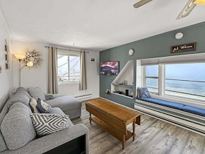 Ein Wohnzimmer mit einer Couch, einem Holztisch und einer Bank, mit Blick auf das Meer.