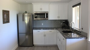 A modern kitchen with white cabinets, a stainless steel refrigerator, a built-in microwave, and a granite countertop.
